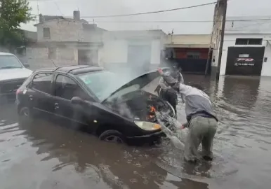 Un auto se prendió fuego en una calle inundada y apagaron el incendio con el agua de la lluvia.